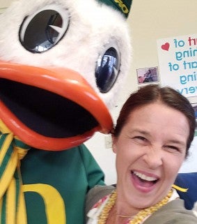 Woman with brown hair laughs next to The Duck, the UO mascot