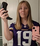 A woman with blonde hair holds a flask and a phone while wearing a Minnesota Vikings football shirt