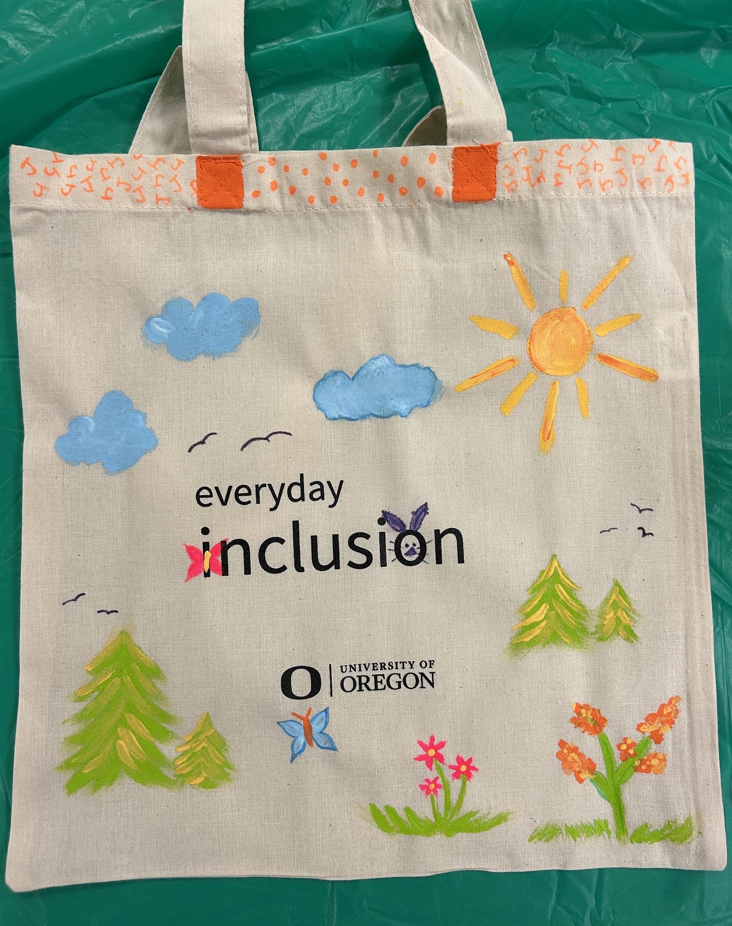 Everyday Inclusion tote bag with clouds, sun, birds, trees, flowers, butterflies, and a rabbit