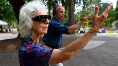 Woman in sunglasses and man in a blue shirt doing tai chi together