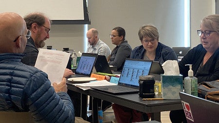 Six seated LEADS participants looking intently at laptop screens and documents while completing a change management simulation