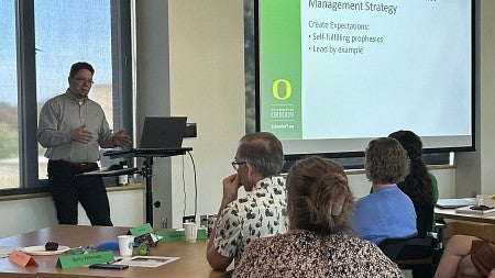 Erik Girvan (white man with brown hair and goatie) leading a conflict management session; slide in the background reads Designing a Constructive Conflict Management Strategy