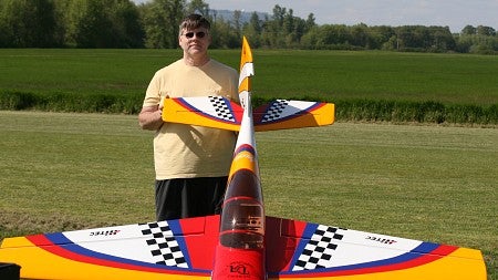 Man in a yellow shirt stands in a green field with a large remote-control plane