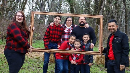 Wanita at left and a man at right hold a picture frame; behind the frame stand three adults and three children
