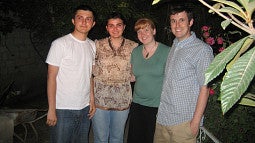 Four people stand together next to a plant; two dark-haired young people next to a red-haired woman and a young cleanshaven Jesse