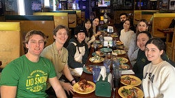 10 interns sit at a long table with plates of pizza slices and salad