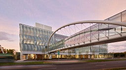 Multi-story building with lots of glass and a walkway traversing a road