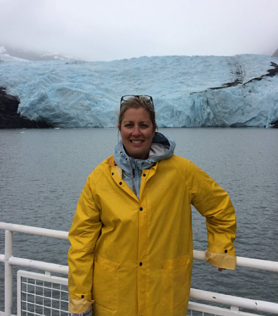 Liz in a yellow jacket standing in front of a railing; behind her is Portage Glacier Chugach National Forest Alaska