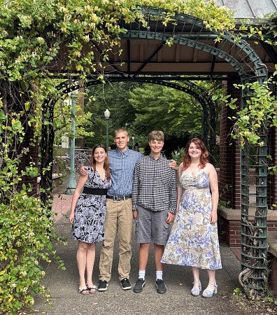 LtoR (Olivia (21), Elliot (19), Ian (15), and Adelaide (17) stand under an arch of vines on UO campus