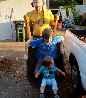 Man and two children playing in a wheel barrow