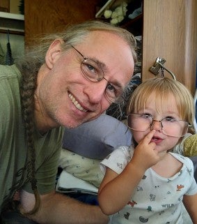 Man with glasses and a green shirt smiles next to a small child with glasses and a white shirt