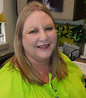 Blonde-haired woman in a light green shirt smiles; Oregon Duck memorabilia behind her.