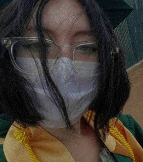 Young white woman with brown hair below her ears, glasses, and a mask, look at the camera