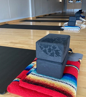 Yoga mats, blanket, blocks, and straps, laid out nicely in a row in a room with a light brown wood floor