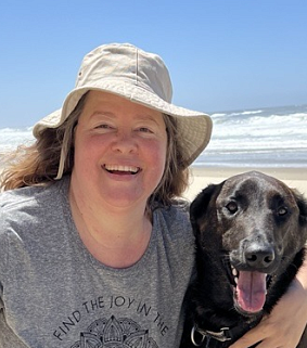 White woman with floppy hat at the beach with her black dog (Stout)