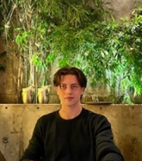 Young white man with short dark hair sitting in front of greenery