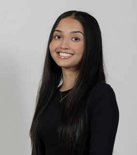 South Asian-American woman with long black hair and wearing a black top looks at the camera with a wide smile; white background
