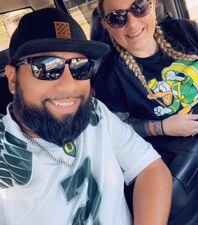 Eric and his wife wearing UO Duck shirts and sunglasses, sitting in a car