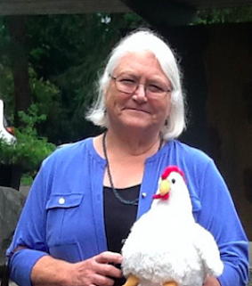 A woman with silver hair and glasses holds a stuffed toy chicken 