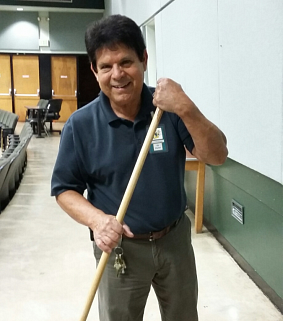 A man stands in a classroom setting holding a broom