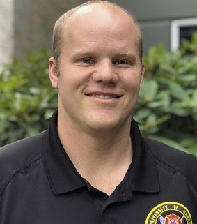 A man wearing a black shirt with a "UO fire marshal 2014" patch smiles at the camera