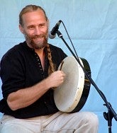 Man holds a bodhran drum in his left hand and plays it with his right