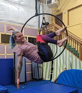Justin Ambron practicing Lyra at Bounce Gymnastics--figure suspended in a hoop hanging above a thick, blue gymnastics mat