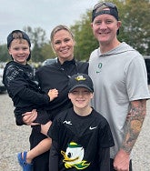 Ashley in center (young woman with blonde hair) carrying a young boy (her son); her husband stands next to her at right; her other son is in front of her in UO wear