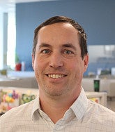 White man with short brown hair smiles at the camera; office cubicles in background
