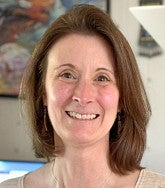 White woman with shoulder-length brown hair smiles at camera