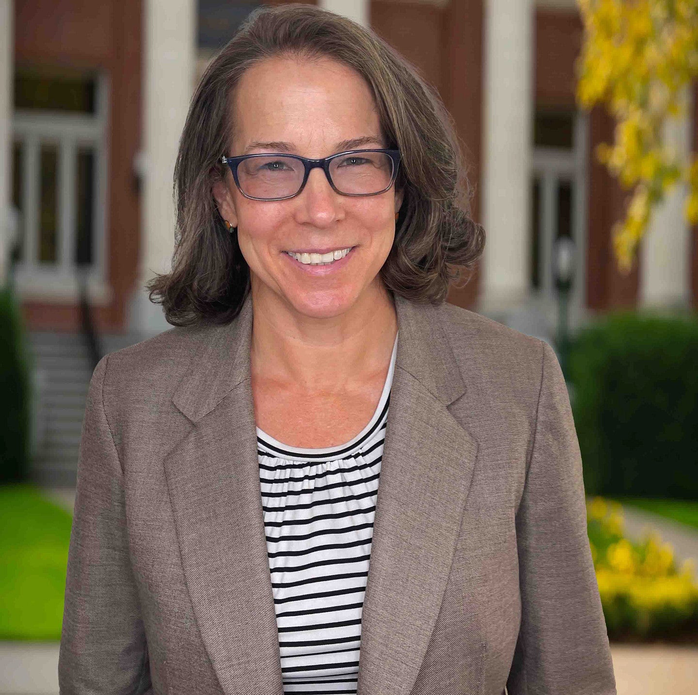 Female with brown hair, glasses, heathered grey jacket 