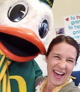 Woman with brown hair laughs next to The Duck, the UO mascot