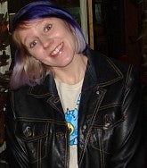 Smiling woman with dark and purple hair smiles at the camera with her head tilted down to the right