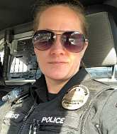 A police officer in uniform, wearing  badge that reads POLICE OFFICER, UNIVERSITY OF OREGON, looks through sunglasses at the camera