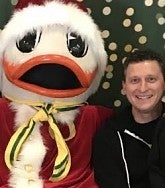 At right: dark-haired man smiles at the camera; at left: the UO duck in Santa attire