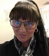 Woman with dark hair and black-rimmed glasses looks at the camera in an office environment
