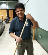A man stands in a classroom setting holding a broom