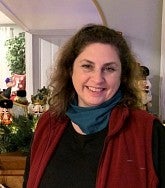 Woman with brown hair smiles in front of Christmas decorations