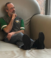 Man in a UO Ducks shirt and jeans sits in an over-sized arm chair looking left