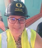 Woman wearing a safety vest, glasses, and a hard hat--the hard hat reads "O Design and Construction"